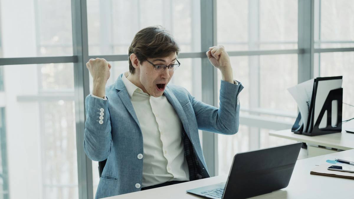 Young businessman using laptop computer receiving good message and become very excited and happy sitting in modern office indoors